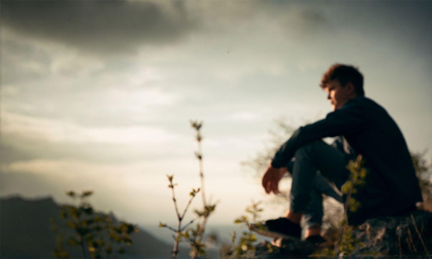 Jeune homme assis au bord d'une falaise rocheuse.