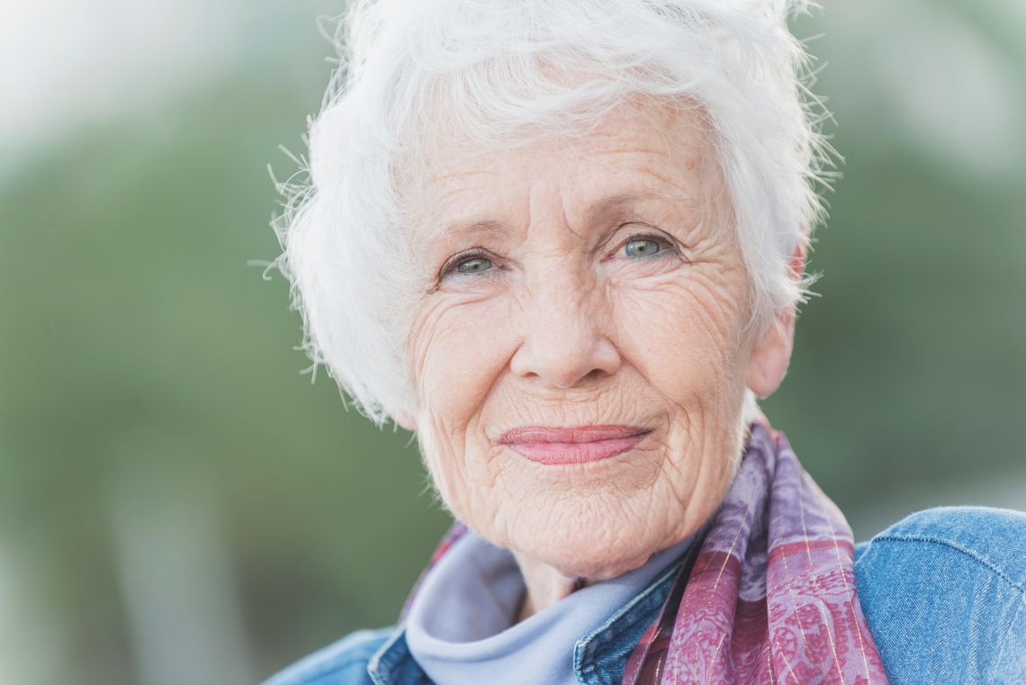 Visage d'une femme âgée de 70 ans, heureuse, aux cheveux blancs et aux yeux bleus, en plein air.