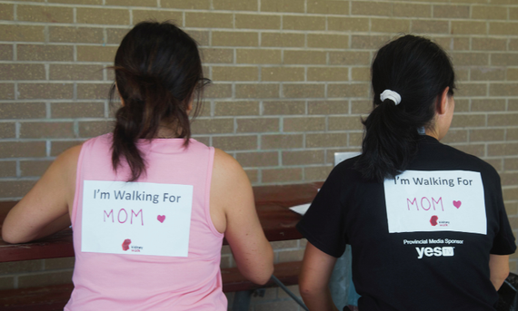 A backview of two women with a sign I'm walking for Mom on their backs