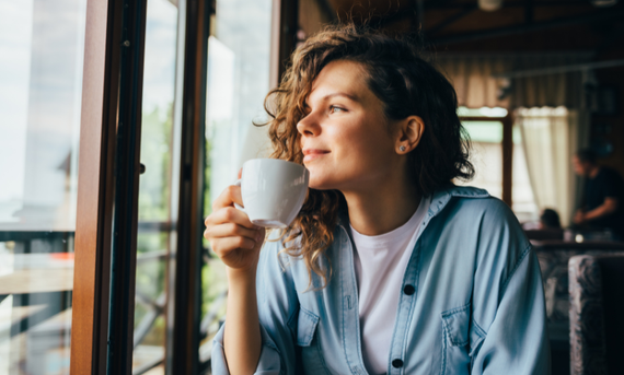 A woman holding a cup of coffee looking through a window