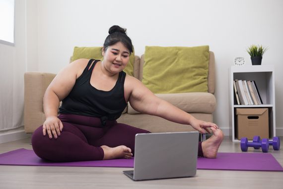A woman doing exercice on a mat in front of her laptop computer