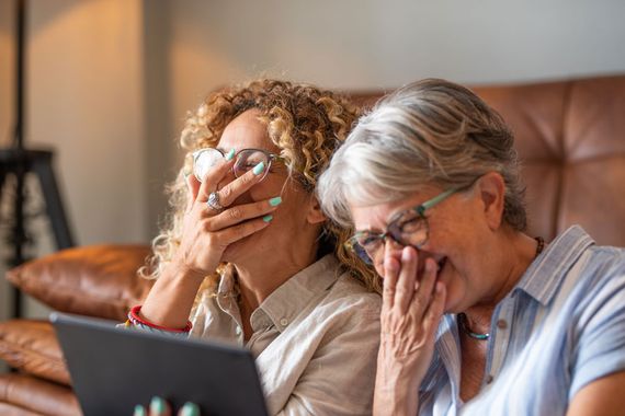 Two women laughing while watching a laptop computer.