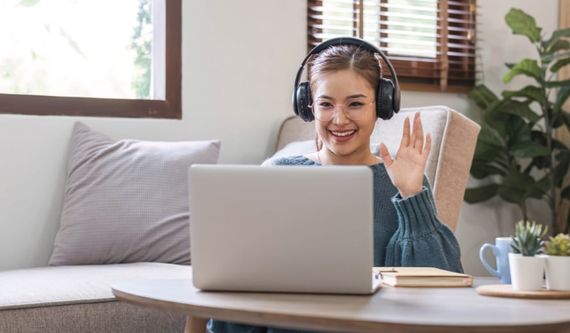 Une femme souriante avec un casque d'écoute fait un signe à l'écran de son ordinateur portable