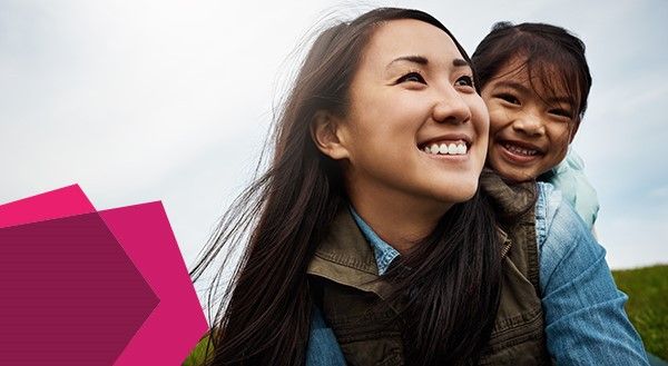 A woman with her child on her back, both are smiling.