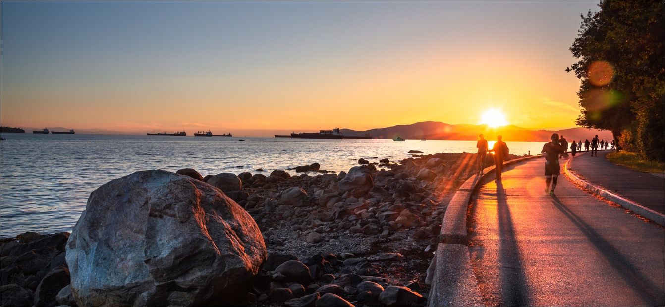 A beautiful view of a lake with a sidewalk an a sunset.