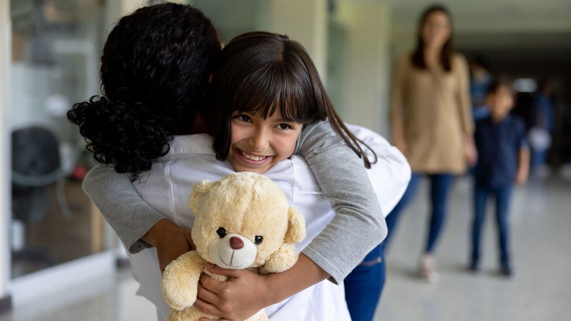 Young daughter in mother's arms, holding a plush bear.