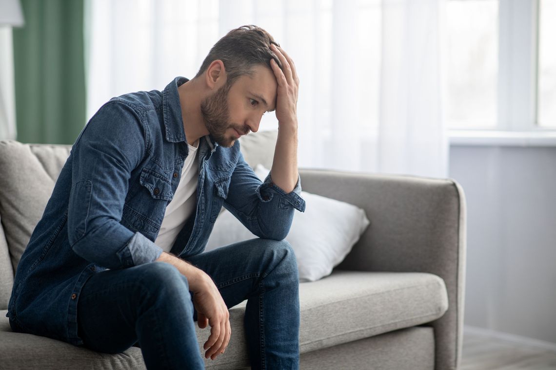 Frustrated middle-aged man sitting on sofa in living room.